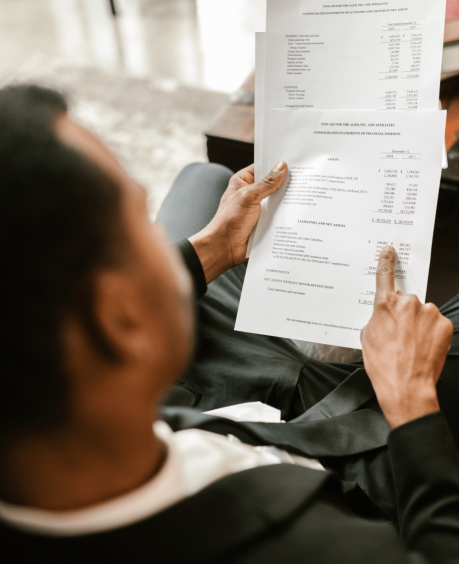 A person in a suit examines financial documents, pointing at a section on a printed page.